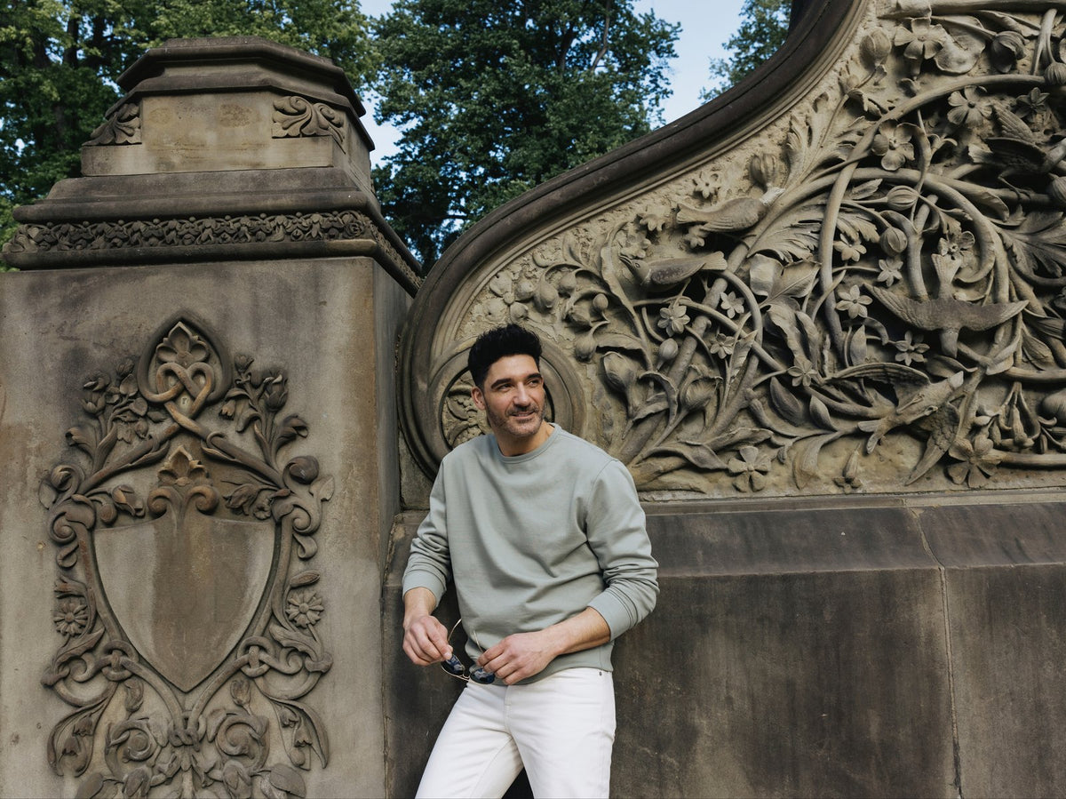 Man in a sage Pima Fleece crew by a carved stone wall