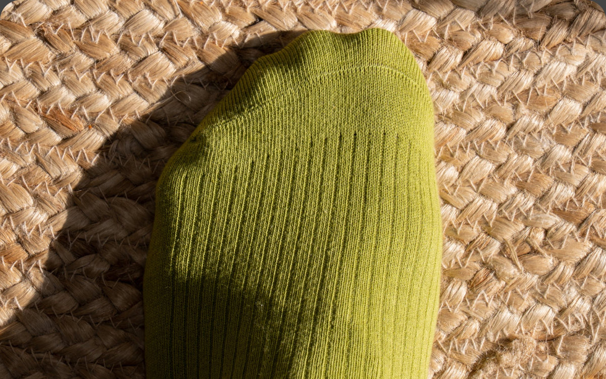 Close-up of a Pickle green ribbed sock toe on a woven jute rug
