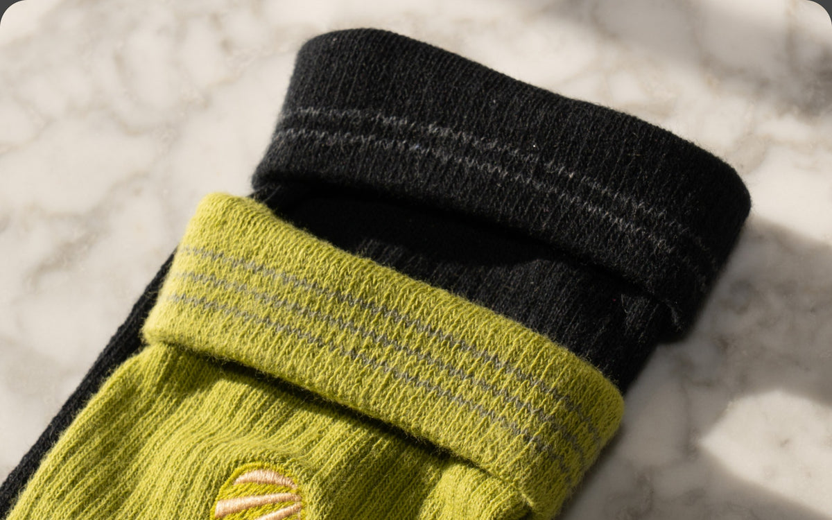 Pickle green and Black Coffee crew socks with cuffs folded down to show the size stripes inside, on white marble