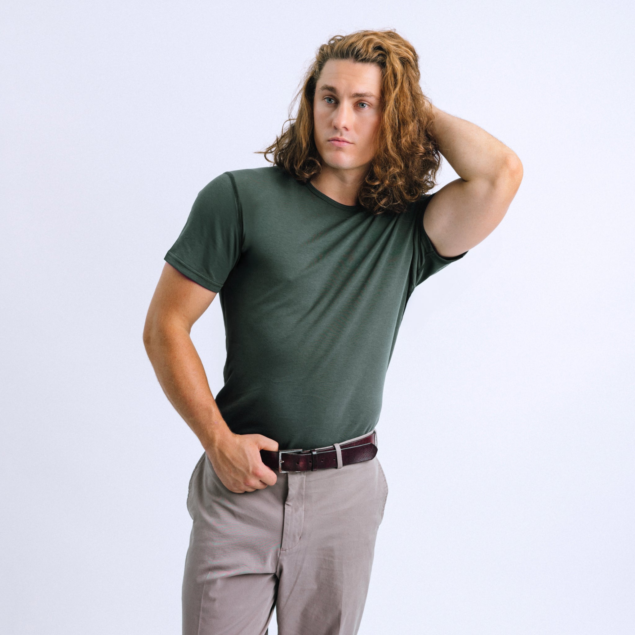 A person wearing a green crew neck t-shirt and beige pants, standing against a white background.