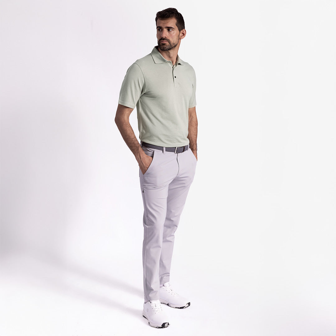 Man wearing a light green polo shirt and gray pants on a plain background