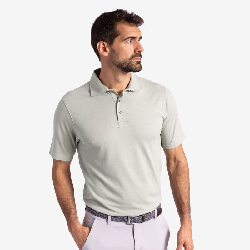 Man wearing a light gray polo shirt and white pants against a plain background.
