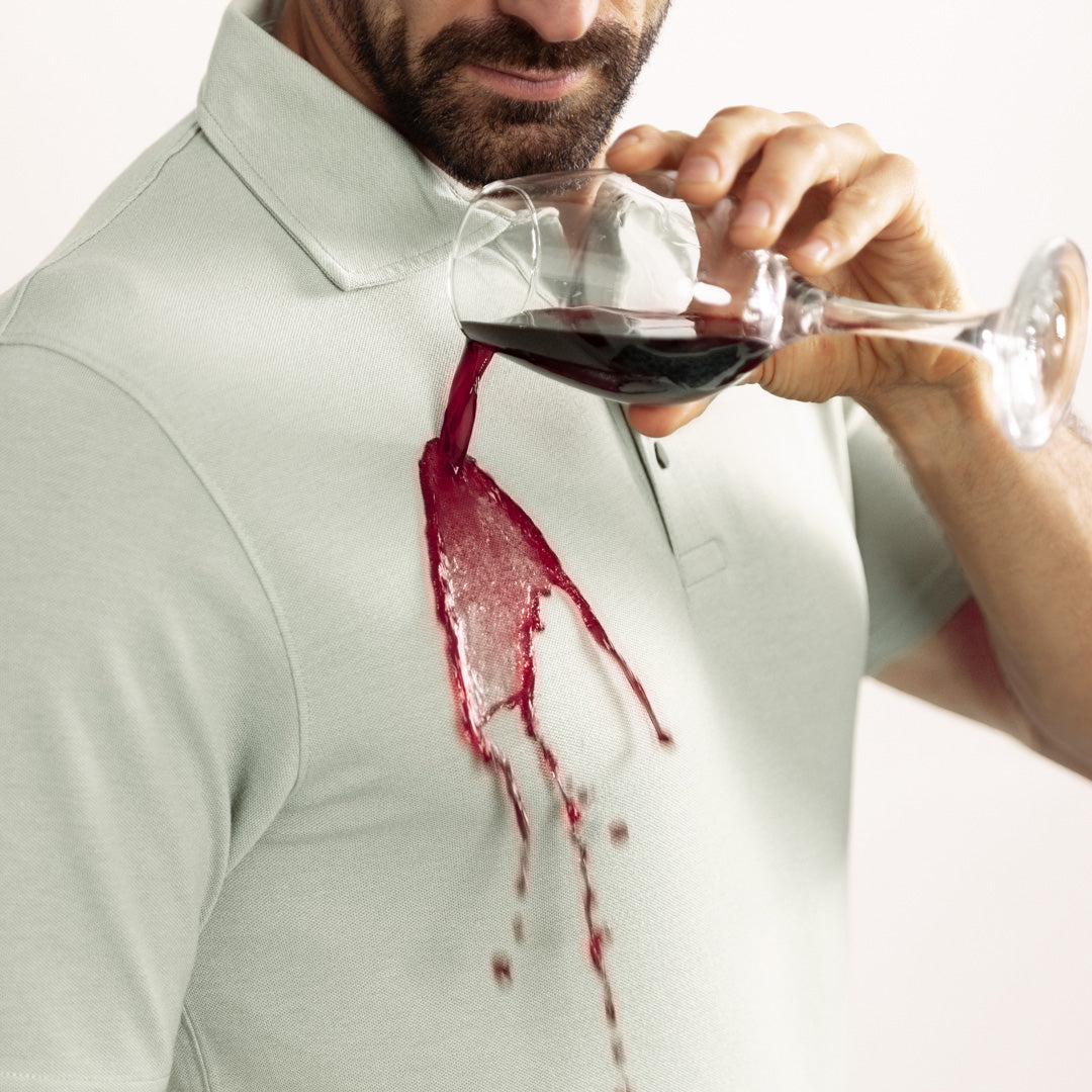 Person pouring red wine into a glass, causing spillage on a light-colored shirt.